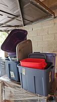 Stack of assorted plastic storage totes including deep blue, grey, purple, and red colors, some with lids.