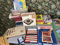 Full view of vintage boxed games laid out including Booby-Trap, Backgammon, Battleship, Michigan Rummy, Brilliant Knight chess set, Wildfire, and more.