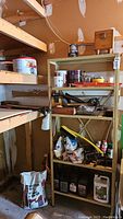 Photo of shelving unit in workshop setting showing bags, paints, tools, and sealant cans on shelves.