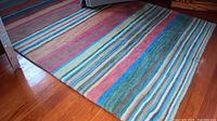 Full view of multicolor striped hand tufted wool pile area rug on hardwood floor showing pattern and colors.