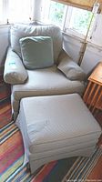 Upholstered arm chair with matching cushion and ottoman visible, fabric in pale gray pattern.