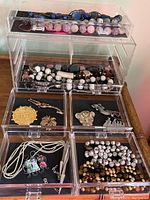 Overall lot showing several acrylic containers filled with artisan jewelry including beaded bracelets, pins, and necklaces
