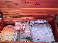 Wooden chest containing folded bed linens in pastel colors such as yellow, light blue, and floral patterns.