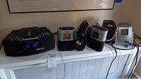 Photo of six clock and radio devices including Frontgate CD player radio, Timex alarm clocks, and Radio Shack emergency radio flashlight.