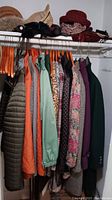 Photo showing various ladies jackets and coats hanging on hangers, including colors like dark green, orange, green, floral print, and purple.