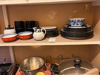 Full shelf view showing stacked plates, bowls, coffee pot, and Asian bowls