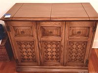Front view of closed wood dry bar cabinet showing decorative carved door panels and three top drawers.