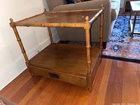 Side angle view of the wooden end table showing bamboo-inspired styled legs and drawer at bottom with metal pull handle.