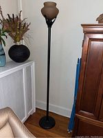 Full view of the tall black metal floor lamp with frosted globe shade beside furniture and decor, showing lamp height and design.