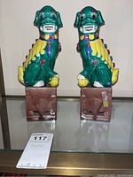 Front view of the pair of ceramic Foo dog figures on a glass surface, showing their vibrant paint and faces.