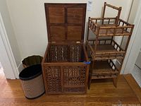 Wooden hamper with lid opened, two waste baskets visible behind it, and rattan shelf to the right.