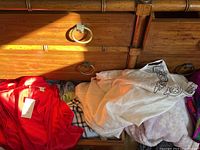 Assorted garments including a red silky item and light colored clothes piled on wooden furniture.