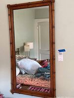 Full rectangular mirror hanging on a wall reflected in the room showing bed and furniture. Framed in faux bamboo wood design.