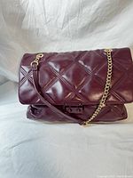 Front view of the quilted wine color Betsey Johnson purse with gold chain strap onto white background.