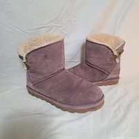 Side angle of the pair of purple suede boots showing the fleece lining and buckle detail at the back, rubber sole visible.