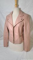 Full front view of a women's blush pink faux leather jacket on a dress form, showing collar, long sleeves, and main two-way zipper.