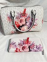 Front view of white GUESS handbag with pink, red, purple floral designs and logo pattern alongside matching wallet.
