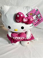 Front view of Hello Kitty plush with pink satin skirt, bow, and heart.