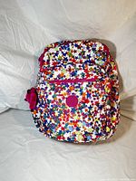 Front view of nylon backpack with multicolored star print, pink zippers, and attached plush monkey keychain.