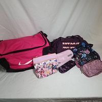 Photo showing the large pink and black Nike duffel bag and an assortment of small cosmetic bags and pouches of various colors and patterns.