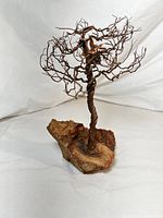 Front angled view of miniature wire bonsai tree sculpture with twisted aluminum branches and copper tone color, mounted on stone base with natural earthy colors.