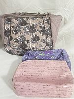 Overall view of the Modern Guess floral patterned handbag and the two cosmetic bags in front, pink with script and purple sequin