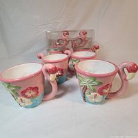 Front and side view of four pink flamingo 3D ceramic coffee mugs with floral and palm tree motifs, showing detailed flamingo handles.