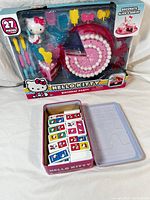Hello Kitty Birthday Party playset and open tin box with domino tiles inside, showing colorful sliceable cake, figure, candles, and serving accessories.