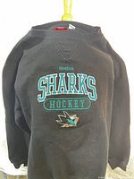 Front view of black Reebok Sharks Hockey sweatshirt showing embroidered text and logo.