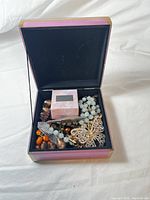 Photo of a box containing multiple beaded bracelets or necklaces of various colors including pale blue, brown, orange, and an ornate butterfly brooch.