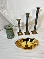 Front angle view showing three candle holders with marble tone shafts and brass tops and bases, the ceramic candle holder, and the polished brass decorative dish on white background.