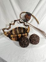 Photo showing vintage rustic woven basket, two dark brown woven decorative balls, and a curved branch with attached small woven star and fabric detail, all arranged on a white backdrop.