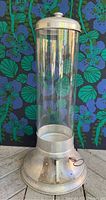 Front view of tall glass cylindrical coffee bean dispenser with metal base and lid, showing overall condition and design.