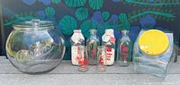 Austin's peanut glass jar, four vintage milk bottles, and yellow-lidded plastic canister displayed together on ground.