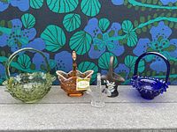 Five glass baskets and decorative glass pieces arranged side by side showing variety in color and design.
