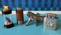 Four unique vintage table top lighters displayed on a blue surface with a blue geometric backdrop.