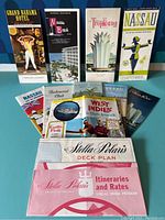 Twelve vintage travel brochures arranged upright and flat showing variety of destinations and titles.