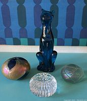 All four pieces displayed together: blue cat figurine, two iridescent paperweights, clear bud vase