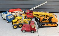 A collection of ten vintage Tonka toy vehicles including front loader, grader, fire truck with ladder, red pickup, dump truck, and tracked excavator with visible wear and paint loss.