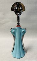 Full front view of corkscrew showing green-blue pleated body and chrome head with smiley face.