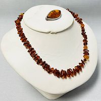 Front view of amber beaded choker necklace displayed on a white bust alongside the amber silver brooch set on top.