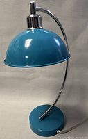 Front view of the vintage blue enamel dome lamp with chrome curved arm and circular base showing minor wear and pull-switch top.