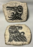 Two Haida stone wall carvings with black stylized bird designs on cracked light stone background, approximate size 6x7 inches each.