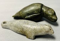 Two soapstone seal carvings on a gray fabric surface, showing the darker green and lighter gray carvings side-by-side