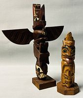 Two carved Native American totem poles side by side, showing relative sizes and details.