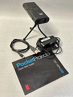 3M MPro150 projector on tripod stand with power adapter, USB cable, and quick start guide displayed.