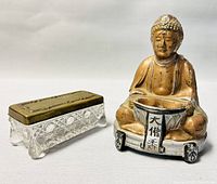 Photo showing metal Asian Buddha figurine with bronze finish next to cut glass trinket box with brass lid.