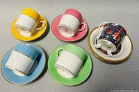 Top and underside view of four Royal Albert demitasse cups and saucers in yellow, pink, blue, and green color bands with gold rims.