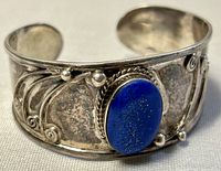 Close-up photo of the front of the silver cuff bangle showing oval Lapis Lazuli stone and detailed silver scrollwork.
