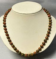 Beaded necklace displayed on white bust stand showing overall length and bead arrangement.